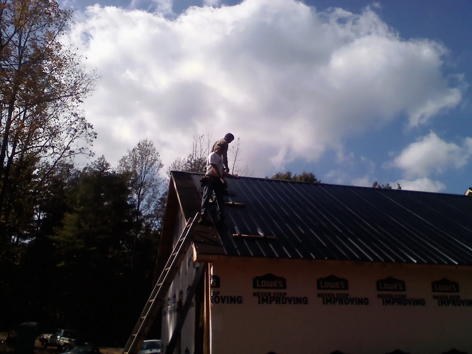 Roofer fastening dark metal panels high against a cloudy sky, from a Roof Inspection job in Nokesville
