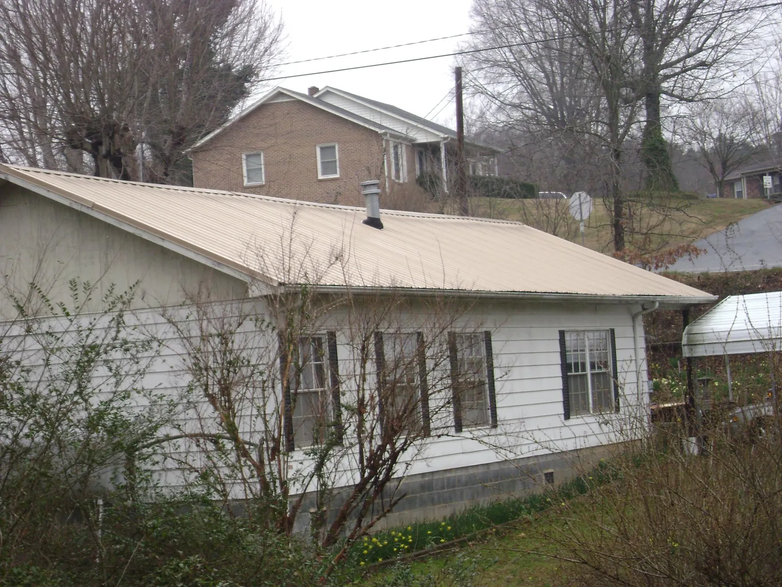 Tan metal roof on a white sided house set into a hillside in Nokesville